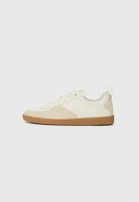 Baltas sneakers, izgatavoti no teksturēta kanvas un zamša materiāla, ar gumijas zoli, noapaļotu purngalu un minimālistisku dizaina akcentiem.