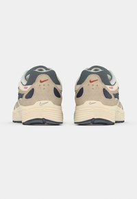 Par bež i mornarsko plavih Nike P-6000 tenisica prikazanih sa stražnje strane na bijeloj podlozi, ističući crvene Nike logotipe i podstavljene potplate.