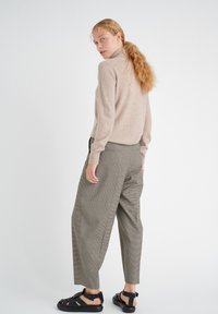 Beige knit sweater with a high neck, paired with gray checkered wide-leg trousers and black strappy sandals, viewed from behind.