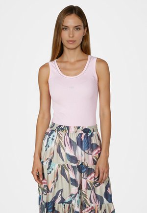 Young woman wearing a light pink sleeveless top and a high-waisted, multi-colored floral skirt, standing against a plain background.