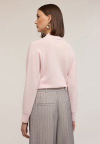 Jasnoróżowy sweter dzianinowy z długimi rękawami, okrągłym dekoltem i ściągaczami na mankietach. Szare spodnie w prążki z tylnymi kieszeniami. Gładka faktura.