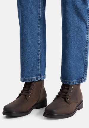 Brązowe skórzane botki za kostkę z sznurowadłami, zaokrąglonymi noskami i gładką fakturą. Noszone z niebieskimi dżinsami o prostym kroju.