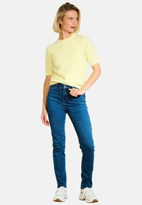 Żółta krótko rękawowa bluzka dzianinowa zestawiona z dopasowanymi niebieskimi dżinsami i białymi trampkami. Prosty design, miękka tekstura i swobodny wygląd.