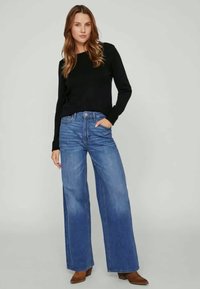 Suéter preto de mangas compridas combinado com jeans azuis de cintura alta e pernas largas. Os jeans apresentam um efeito desgastado e um design clássico de cinco bolsos.