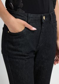 Zwarte denim broeken met een aansluitend ontwerp, achter- en voorke pockets en een gouden knoopsluiting in de taille. Gladde textuur.