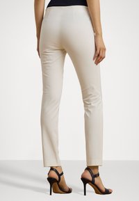 Crème-kleurige fitted broek met een gladde textuur en een taps toelopend ontwerp, gecombineerd met zwarte strappy hoge hakken.