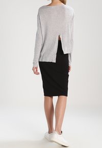 Světlé šedé triko s dlouhým rukávem a hlubokým výstřihem vzadu, spárované s těsnou černou sukní a bílými teniskami, zobrazené z pohledu zezadu.