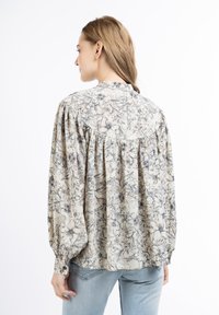 Blumenmuster-Hemdbluse in hellbeige mit blauen und braunen Mustern; verfügt über puffärmel und Rüschen am Rücken und an den Schultern.