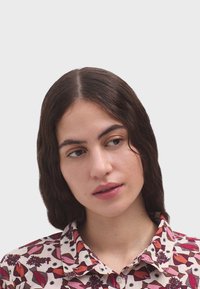 Camisa de cuello con un estampado floral en tonos de rojo, rosa y negro sobre un fondo claro; textura suave y un brillo sutil.