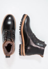 Bottes en cuir noir avec des accents beiges, bout rond, design à lacets et semelles en caoutchouc texturé pour une meilleure adhérence. Doublées d'un matériau doux et gris.