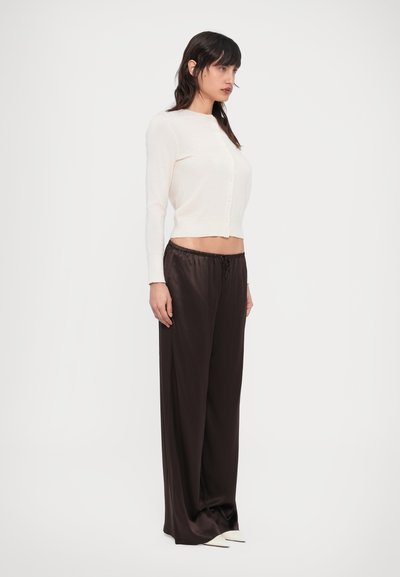 Light beige cropped cardigan with long sleeves and button closure, paired with dark brown satin wide-leg pants featuring a drawstring waist.