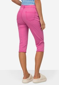 Pantaloni rosa a vita alta con tasche posteriori e orlo sfrangiato, realizzati in cotone. Abbinati a scarpe slip-on color crema.