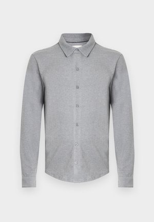 Chemise grise à manches longues en tissu doux, avec un col à revers, une fermeture boutonnée sur le devant et un ourlet arrondi. Design simple sans motifs.