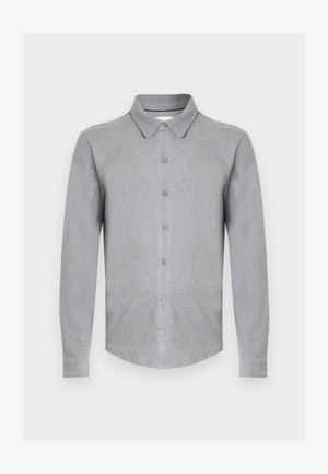 Chemise grise à manches longues en tissu doux, avec un col à revers, une fermeture boutonnée sur le devant et un ourlet arrondi. Design simple sans motifs.