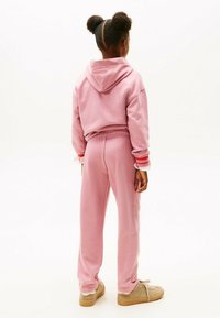 Roze katoenen hoodie met een kangoeroezak en bijpassende joggingbroek. De aangesloten mouwen tonen rode en witte strepen. Tan sneakers maken de outfit compleet.