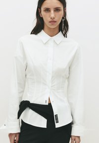 Witte blouse met lange mouwen, een kraag, een slim fit ontwerp, verticale naaddetails en een zwarte stoffen strik om de taille.