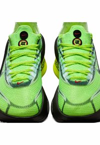 Heldere groene sportschoenen met een getextureerde gebreide bovenzijde, zwarte accenten en een zichtbare gele Zoom Air-unit bij de hiel. Rode Nike-logo detail.