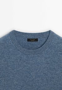 Pull bleu clair avec un col rond, un col côtelé et une texture douce. L'étiquette indique "Fabriqué en Chine" avec une étiquette noire.