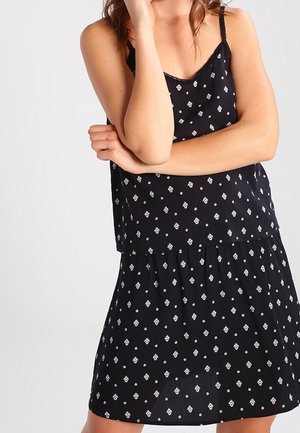 Abito nero senza maniche con un design a strati, caratterizzato da un motivo geometrico bianco e un tessuto leggero. Accentuato da spalline sottili.