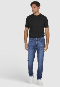 Męskie granatowe dżinsy o prostym kroju, w połączeniu z czarną koszulką z krótkim rękawem i białymi trampkami. Swobodny i wszechstronny strój.