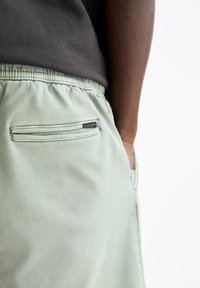Shorts vert clair avec taille élastique, dotés d'une poche arrière zippée et d'une petite étiquette de marque. Tissu doux et design décontracté.