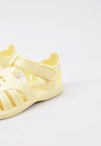 Light yellow sandal made of soft plastic, featuring cut-out design, adjustable strap, and textured sole for grip. Brand "igor" visible.