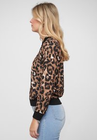 Giacca bomber con stampa leopardata, caratterizzata da un tessuto lucido marrone e nero, polsini neri a coste e una vestibilità comoda.