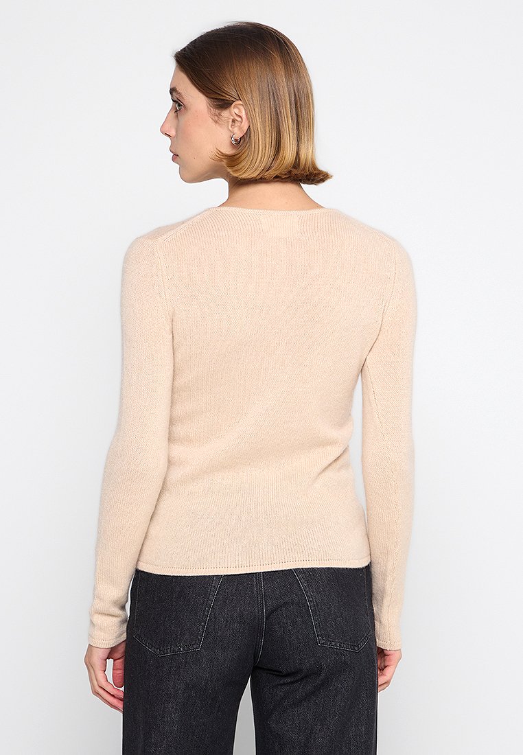 Hellbeiger Pullover mit feiner Strickstruktur, langen Ärmeln und Rundhalsausschnitt, kombiniert mit dunklen, hochgeschnittenen Jeans.