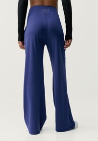 Navyblå byxor med vida ben i ett slätt, stretchigt tyg och hög midja. Har minimala sömmar och en dold logotyp på baksidan.