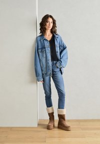 Denimjacka i ljusblått, oversized passform, bärs över en svart ribbad topp. Blå skinny jeans och bruna mockastövlar med fårskinnskant.