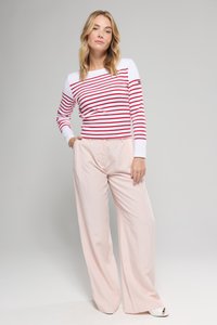 Haut à manches longues rayé rouge et blanc associé à un pantalon large rose pâle. Le haut présente un col rond et des manches ajustées. Chaussures blanches ouvertes.