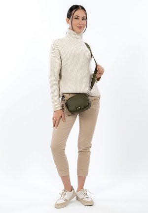 Groene getextureerde crossbodytas met verstelbare riem, gecombineerd met een crème geribbelde coltrui en beige cropped broek. Witte sneakers gedragen.