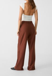 Bruine hoge taille wijde broek met elastische band. De stof lijkt zacht en vloeiend, gecombineerd met een strakke witte top.