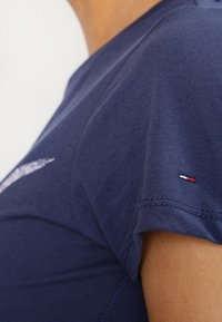 Marinblå bomullströja med korta ärmar, rund halsringning och en liten logotyp med röda, vita och blå detaljer på ärmvrån.