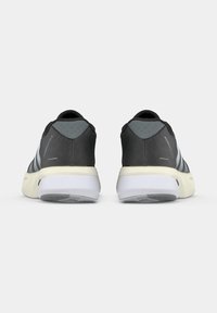 Paire de chaussures de course noires et grises avec semelles blanches vues de dos sur un fond clair uni.