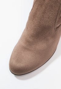 Bota corta de ante marrón con punta redondeada y textura suave. Cuenta con un tacón bajo y líneas limpias, adecuada para diversos conjuntos.