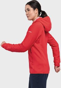 Rote, strukturierte Kapuzenjacke mit Reißverschluss und Seitentaschen, die ein tailliertes Design und ein Logo auf der rechten Schulter aufweist.