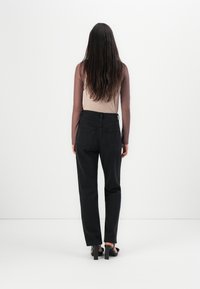 Black high-waisted pants with a straight-leg cut, paired with a long-sleeve brown top. Smooth fabric with a simple design and no visible patterns.
