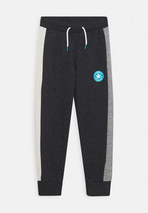 Ciemnoszare spodnie dresowe z białymi i szarymi panelami bocznymi, elastycznym pasem z białymi sznurkami oraz niebieskim logo Converse All Star na lewym udzie.