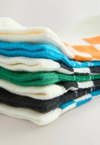 Pile de pulls en maille pliés en blanc, orange, bleu, vert et gris foncé sur une surface unie avec un éclairage doux.
