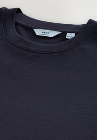 Marinblå T-shirt med rund hals och etikett som visar varumärket "NEXT" och "Relaxed Fit", storlek medium, tillverkad i Bangladesh.