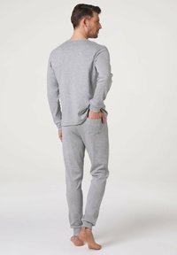 Maglietta grigia a maniche lunghe e pantaloni della tuta, realizzati in tessuto morbido. La maglietta ha un collo rotondo; i pantaloni presentano polsini elasticizzati e tasche laterali.