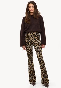 Pantalones acampanados con estampado de leopardo en suave tejido marrón y negro, combinados con un suéter acolchado de color marrón oscuro. Presenta una cintura alta y piernas largas y anchas.