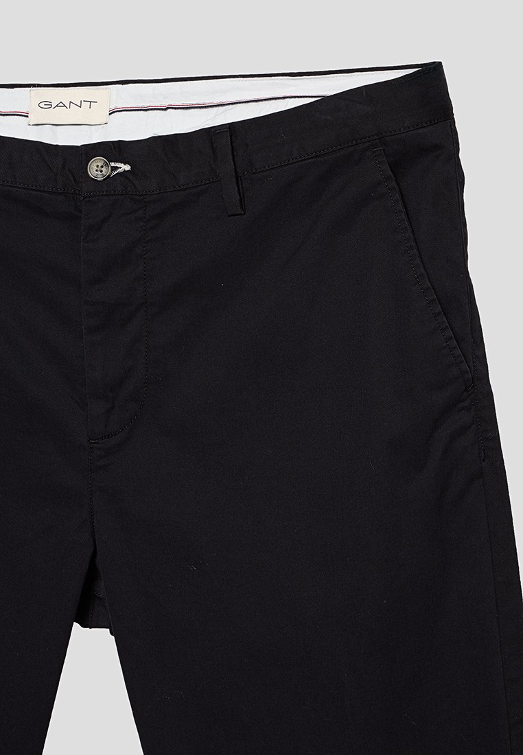 Chino neri in cotone con frontale piatto, tasche standard e chiusura a bottone. Presentano una fodera in vita bianca con dettagli rossi e blu.