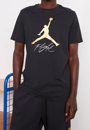 Black cotton T-shirt featuring a large gold "Jumpman" logo and the word "Flight" in a cursive font. Short sleeves and crew neck design.