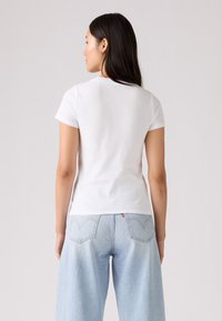 Hvid bomulds T-shirt med korte ærmer, rund halsudskæring og tætsiddende design, parret med lyseblå denim jeans med baglommer.