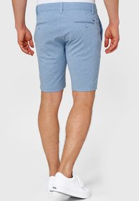 Lyseblå shorts lavet af tekstureret stof, med to baglommer med knapper og en skræddersyet pasform. Bruges med hvide sneakers.