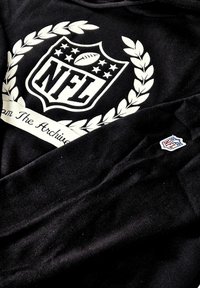 Black sweatshirt featuring a large white NFL logo with laurel wreath design. Small embroidered NFL logo on the right sleeve. Soft texture.
