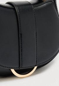 Μαύρη δερμάτινη τσάντα με χρυσά κυκλικά μεταλλικά στοιχεία, με λείο υφή και αντίθετες ραφές, δημιουργώντας ένα κομψό, μοντέρνο σχέδιο.