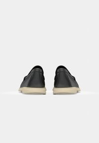 Black leather slip-on shoes with a rounded toe and beige rubber sole. Smooth texture with minimal design and no visible logos.